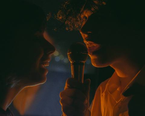 Two singers sharing one microphone in amber light